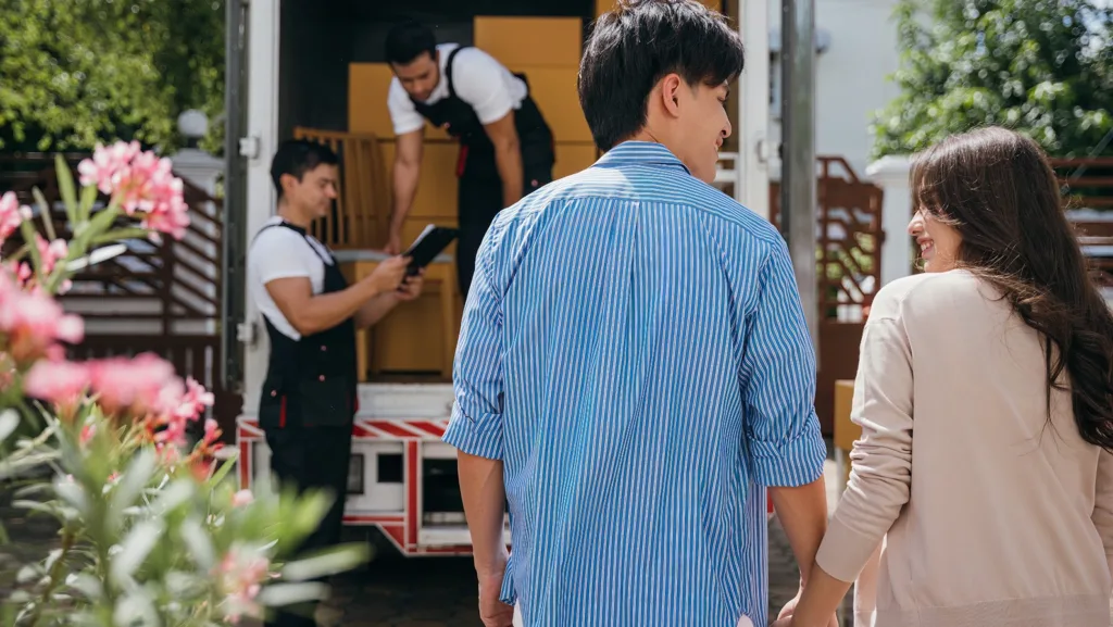 Assisted by a professional delivery team a couple transitions to their new home. Together they unload and lift cardboard boxes ensuring an organized and efficient move. Moving Day Concept