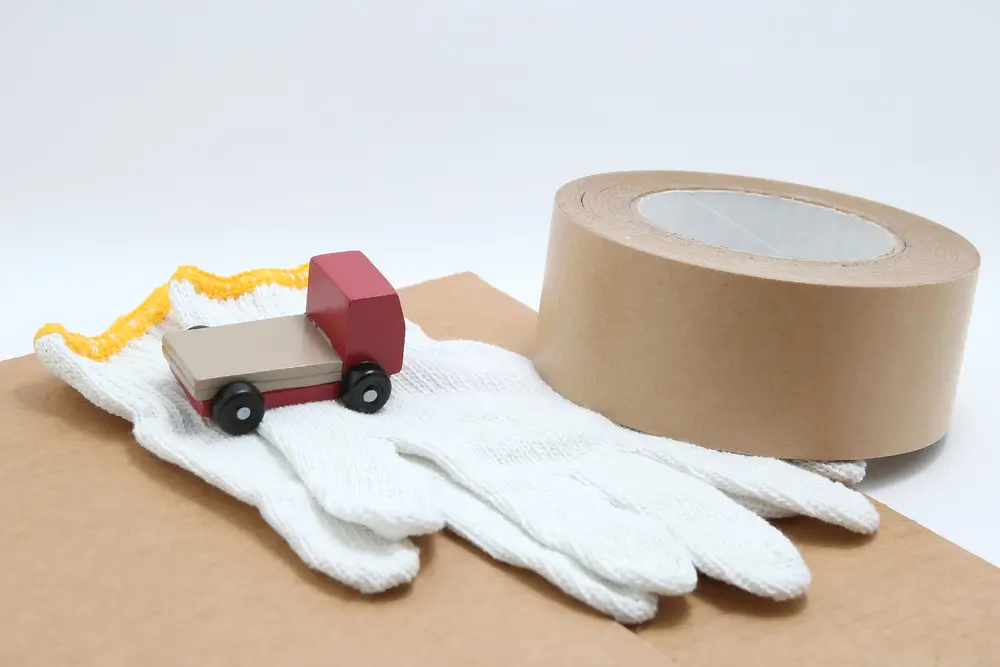 Toy mini car truck, packing tape, card boards, and cotton work gloves on white background. 