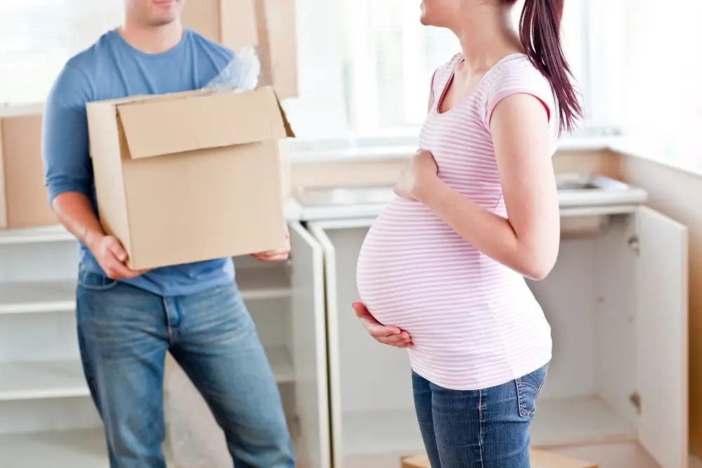 Close-up of a pregnant woman talking to her husband who is carrying a box in their new house