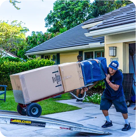 A man pushing a cart loaded with a box, moving forward in a well-lit environment.