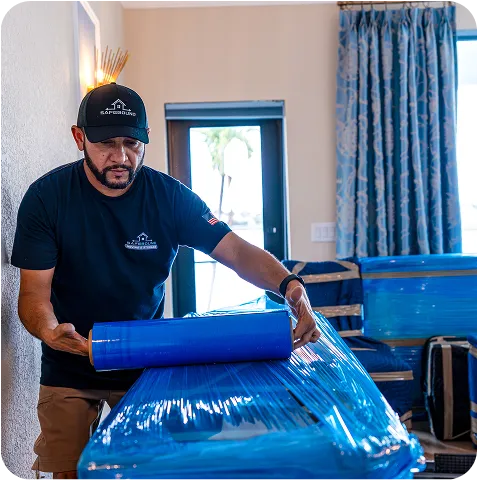 A man wearing a blue shirt is wrapping furniture for protection.
